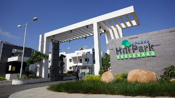 Entrance gate of Aparna HillPark Boulevard with modern architecture, security gate, landscaped greenery, and residential community buildings in Hyderabad.