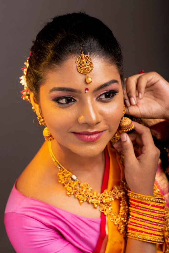 Portrait of a smiling Indian woman in traditional attire and jewelry indoors.